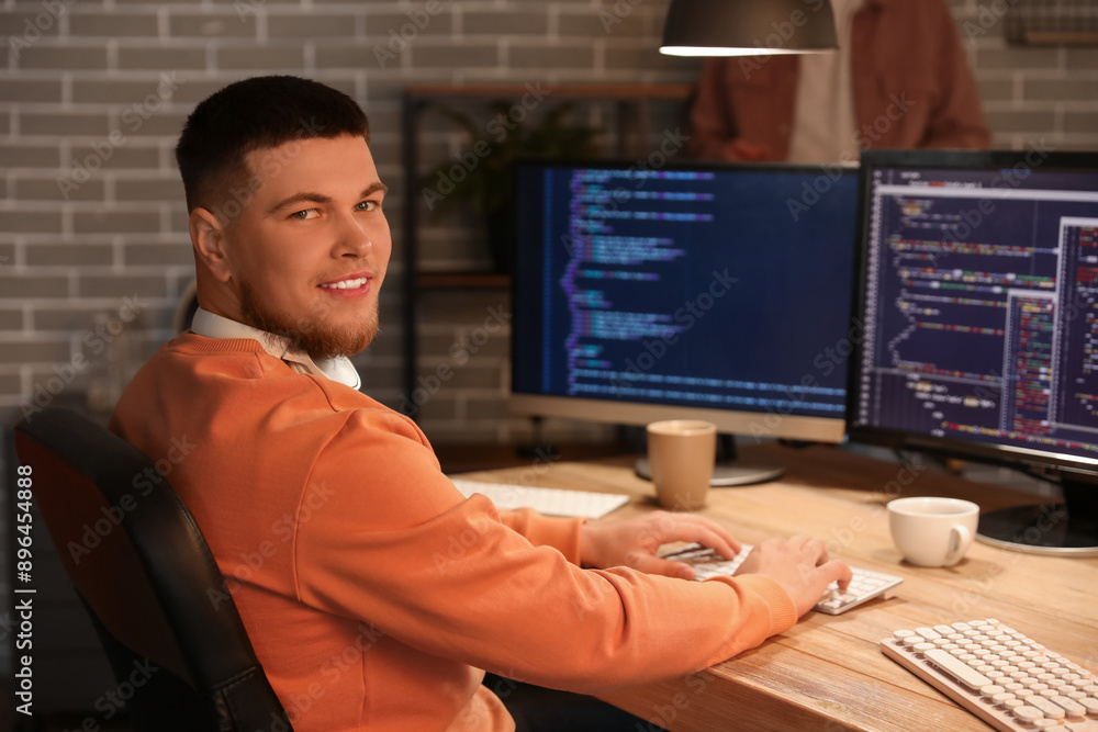 Poster male programmer working with computer in office at night