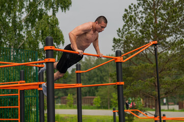 Fototapeta premium A shirtless man is doing a workout on the horizontal bars outdoors.