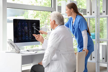 Obraz premium Mature doctor with nurse studying MRI scan on computer screen in clinic