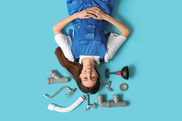 Happy young female plumber with  plumbing items lying on blue background