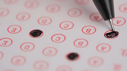 Female circles correct answers in standard exam test paper with black pen. Student filling up the answer sheet, coloring right answer, macro shot.