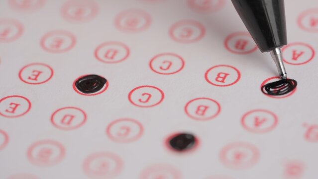 Female circles correct answers in standard exam test paper with black pen. Student filling up the answer sheet, coloring right answer, macro shot.