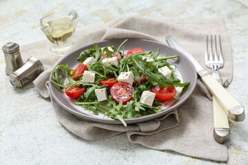 Plate with healthy vegetable salad, napkin and cutlery on light grunge background