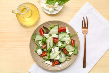 Plate of fresh vegetable salad with feta cheese cubes and fork on wooden background