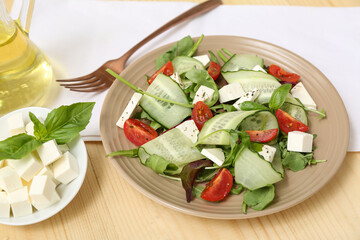 Plate of fresh vegetable salad with feta cheese cubes and fork on wooden background