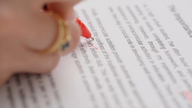 Professional school or college teacher grades a homework exam papers of students. Woman checks essay and crosses wrong word, corrects it with red pen.