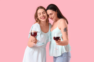 Beautiful young lesbian couple with glasses of wine on pink background