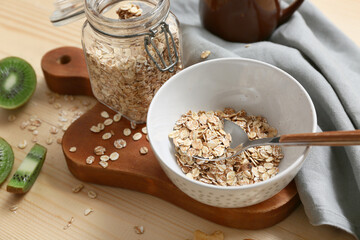 Napkin, kiwi and bowls with raw oatmeal on wooden background