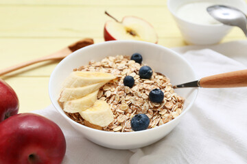 Napkin, fruits, berries and bowl with raw oatmeal on yellow wooden background, closeup