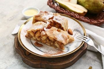Plate with pieces of tasty pear strudel and fork on grunge grey background