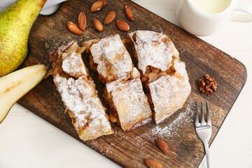 Wooden board with pieces of tasty pear strudel and fresh fruits on light background