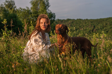 young cheerful woman playing with her dog outdoors in beautiful countryside field. Female and ridgeback dog walking and having fun