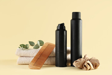 Hair spray with comb, scrunchy and towels on light yellow background