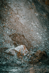 a large stone with red inclusions lying near a clay hill, close-up