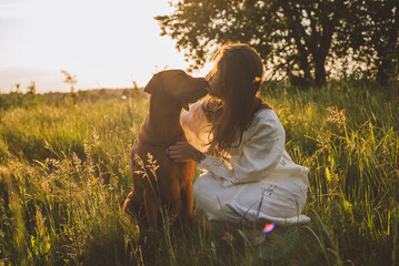 young cheerful woman playing with her dog outdoors in beautiful countryside field. Female and ridgeback dog walking and having fun