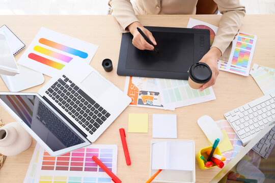 Female graphic designer with tablet and coffee working at table in office, top view