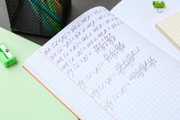 Copybook with math formulas and stationery on table, closeup