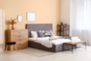 Comfortable bed, shelving unit, chest of drawers and bench in interior of bedroom. Blurred view