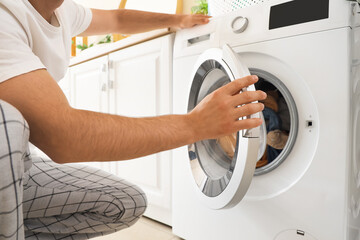 Young man using washing machine in laundry room