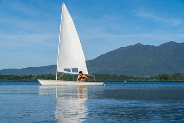 Young person enjoying a beautiful summer day while sailing a laser sailboat on Lake Panguipulli.