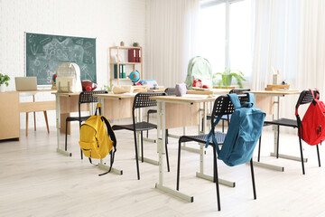 School desks with backpacks and blackboard in light classroom