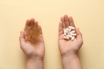 Hands with clump of hair and pills on beige background. Hair loss problem