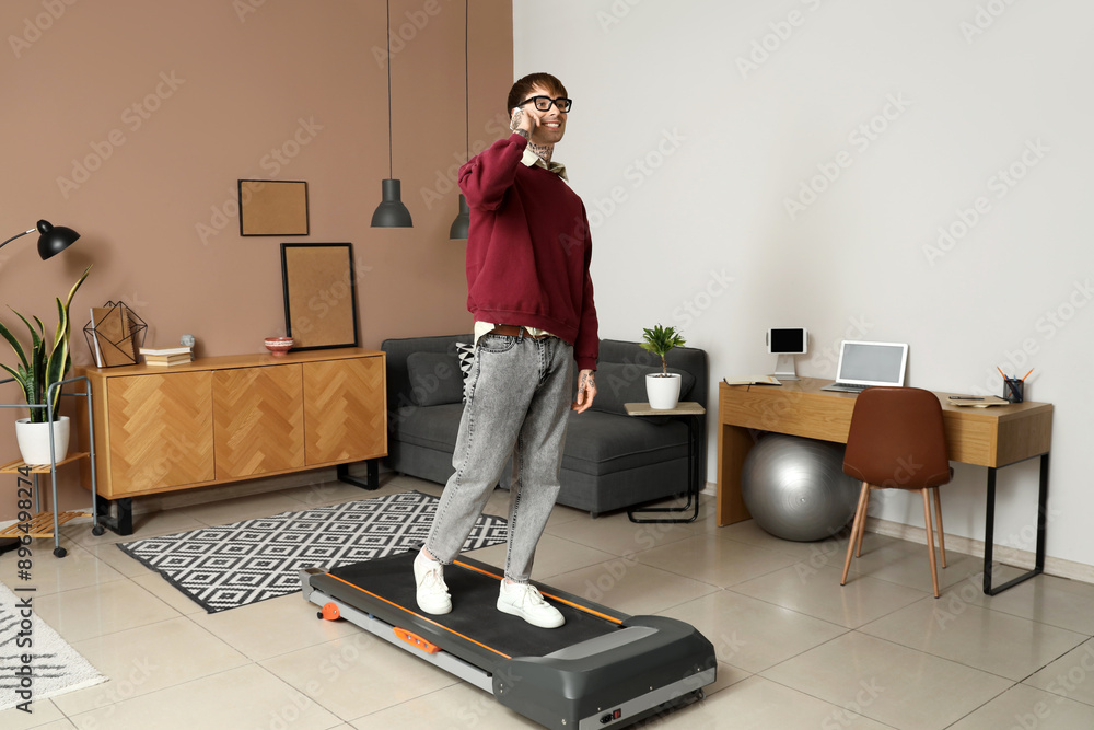 Wall mural young businessman talking by mobile phone on treadmill in office