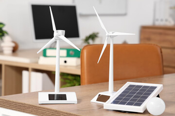 Wind turbine models with portable solar panel and light bulb on engineer's table in office, closeup