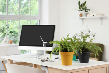 Engineer's workplace with computer monitor, plants and wind turbine model in office