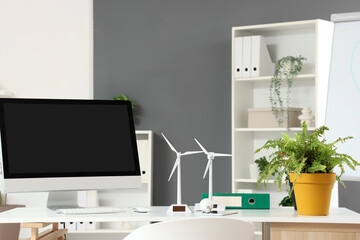 Engineer's workplace with computer monitor, plant and wind turbine models in office
