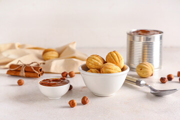 Bowls with tasty walnut shaped cookies, boiled condensed milk and hazelnuts on white wooden table