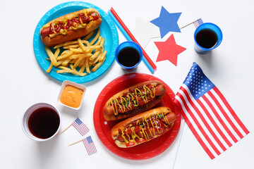 Tasty hot dogs with USA flags, cola and french fries on white background. American Independence Day celebration