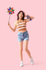 Young Asian woman in bucket hat with toy windmill on pink background