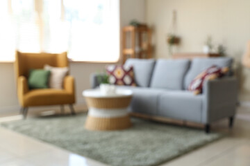 Blurred view of living room with grey sofa, coffee table and armchair