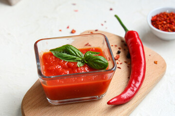 Glass bowl of tomato sauce with basil and chili pepper on white background