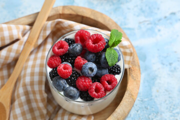 Glass of tasty yogurt with different fresh berries and mint on light blue background