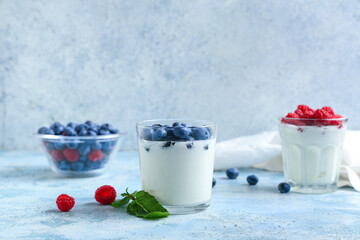 Glasses of tasty yogurt with fresh blueberries and raspberries on light blue background