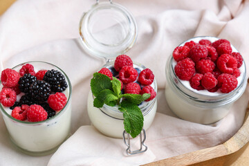 Glass and jars of tasty yogurt with different fresh berries on table, closeup