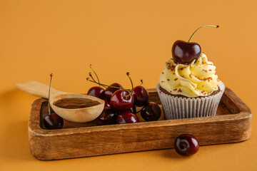 Wooden board with sweet cherry cupcake and spoon of jam on brown background