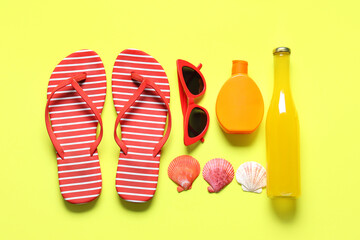 Stylish striped flip-flops with bottle of cocktail, sunglasses, seashells and sunscreen cream on yellow background