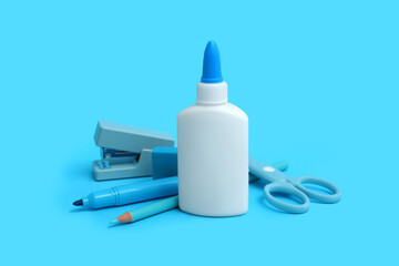 Bottle of glue, scissors and stapler on blue background
