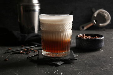 Glass of White Russian cocktail and bowl with coffee beans on black background
