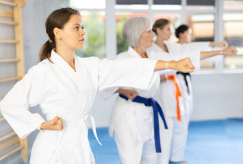 Women of different ages in kimono trying new martial moves at karate class