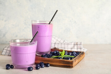 Glasses of fresh blueberry smoothie and wooden board with berries and mint on white background