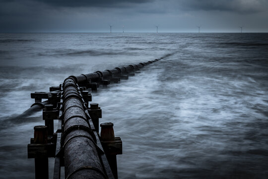 Corroded iron pipe, sewage pipe in the sea surf under a dark sky, Blyth, Northumberland, Great Britain