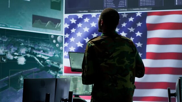 Professionals in US military uniforms operate computers and big screen, working on surveillance and intelligence to ensure national security from a high tech control center. Camera A.