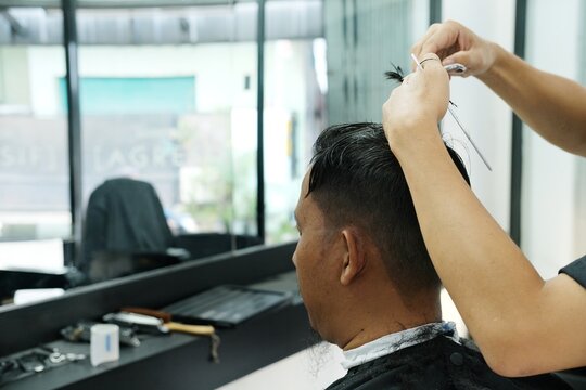 A man getting his hair trimmed in a barbershop. The barber's hands skillfully cut the hair with scissors. Perfect for advertising grooming services, barbershops, and hairstyling tutorials.