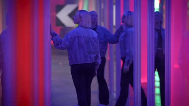 A woman in a neonlit mirror maze, enjoying a colorful and futuristic art installation