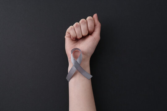Woman with grey awareness ribbon on black background, top view