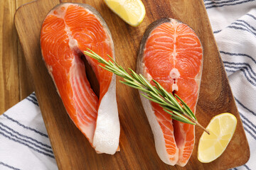 Fresh salmon steaks, lemon and rosemary on wooden table, top view